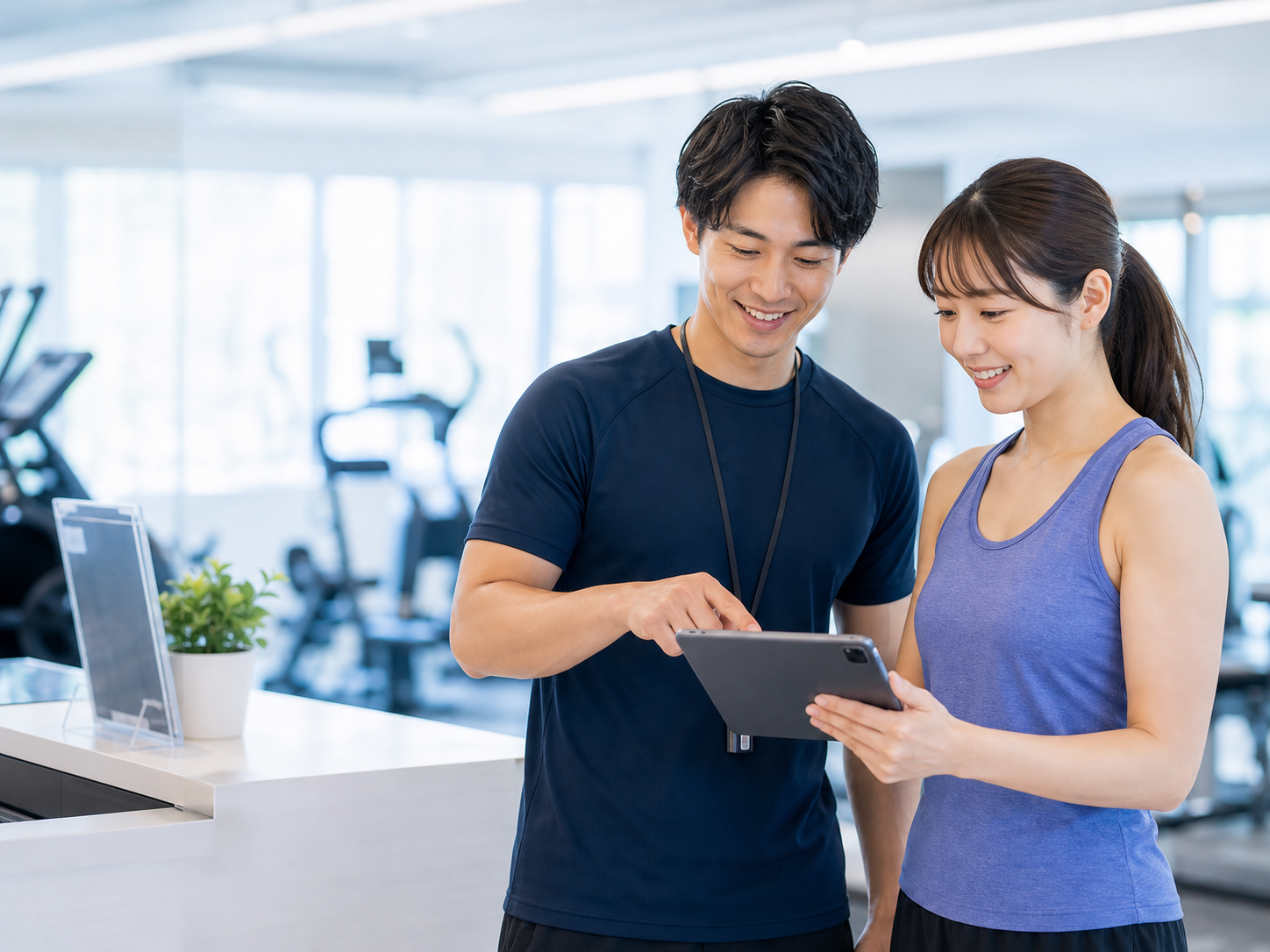 ジムでトレーナーと会員がタブレットを確認している様子